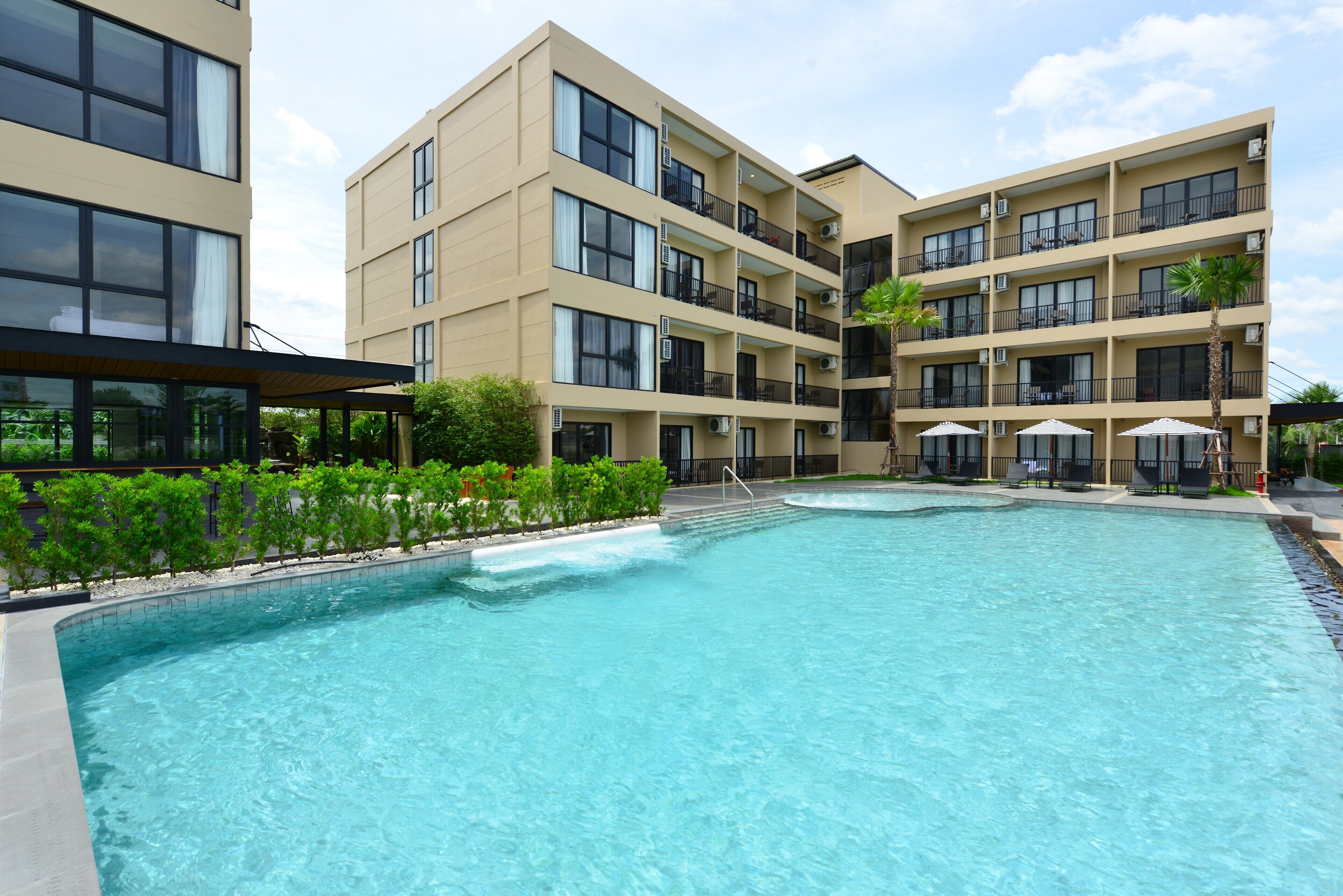 A modern hotel with a large outdoor swimming pool, multiple balconies, and outdoor seating areas.