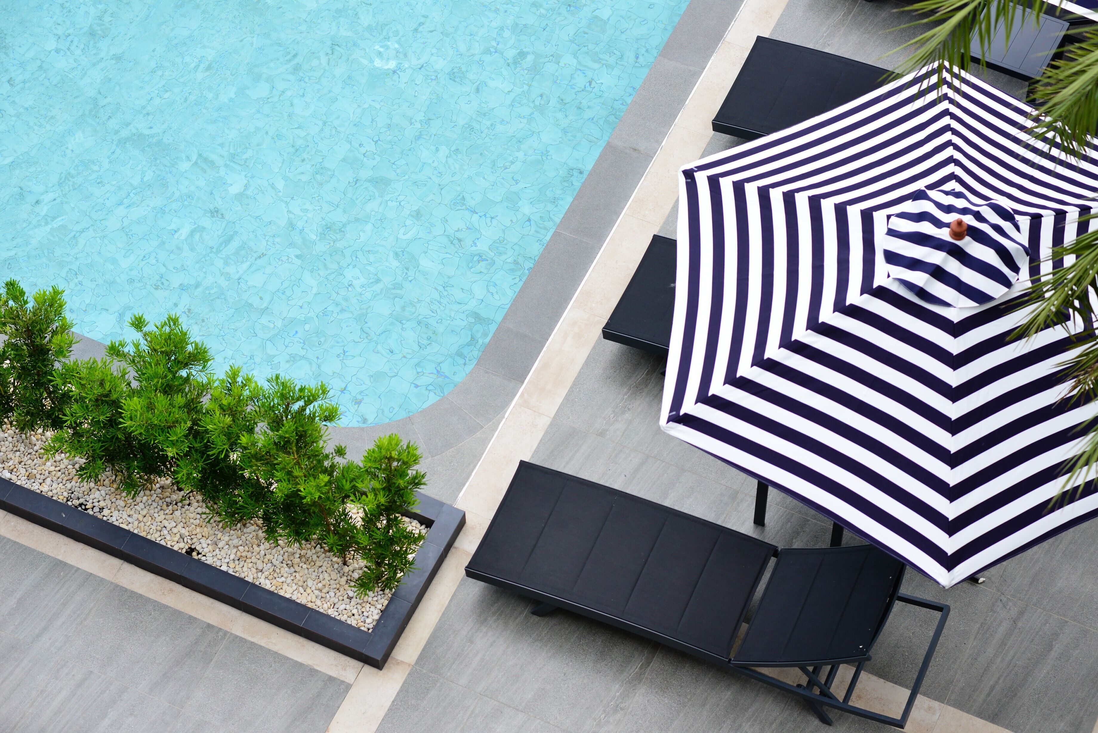 A poolside area with a swimming pool, lounge chairs, and a striped umbrella.