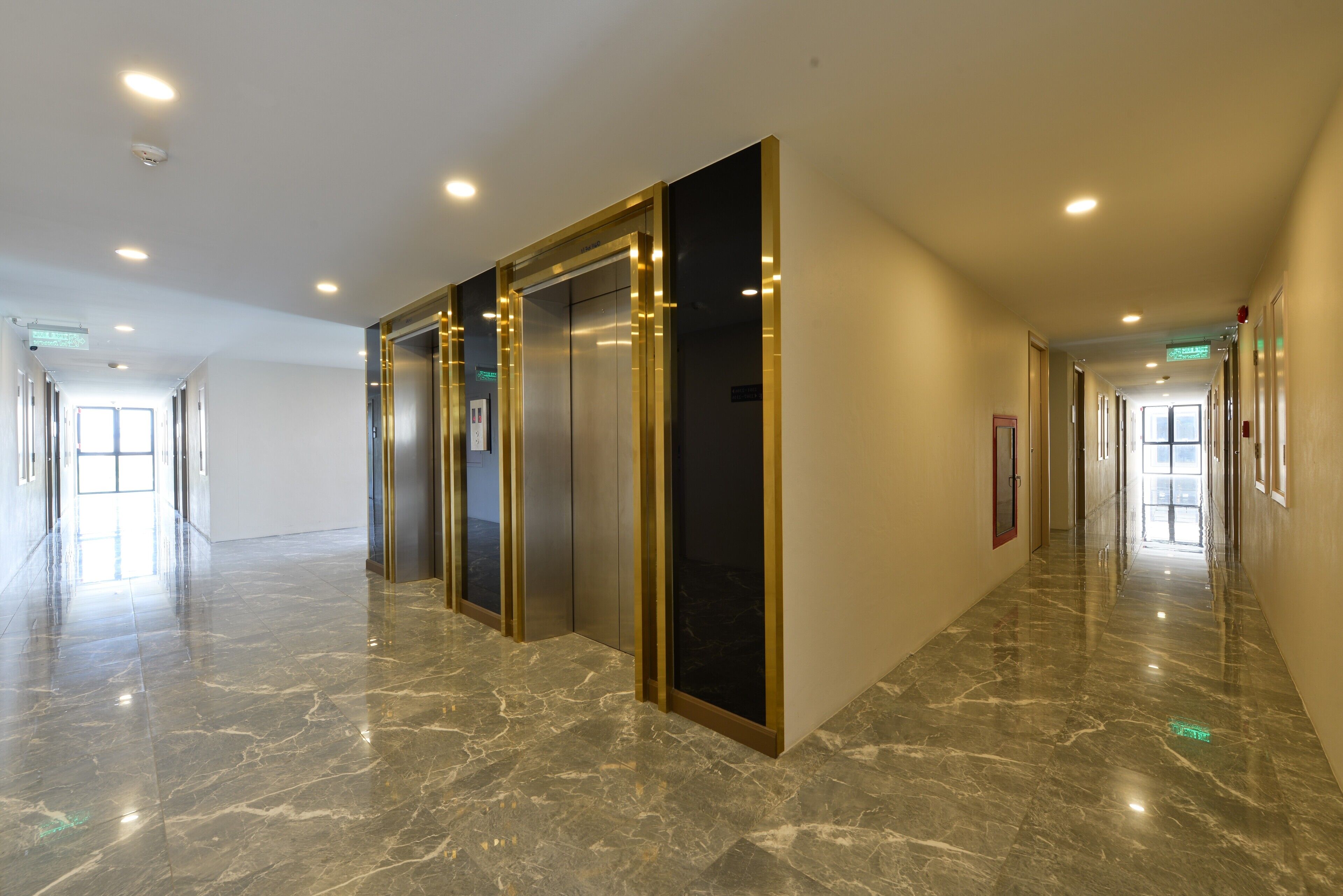 A spacious, well-lit hallway with marble flooring and modern elevators.