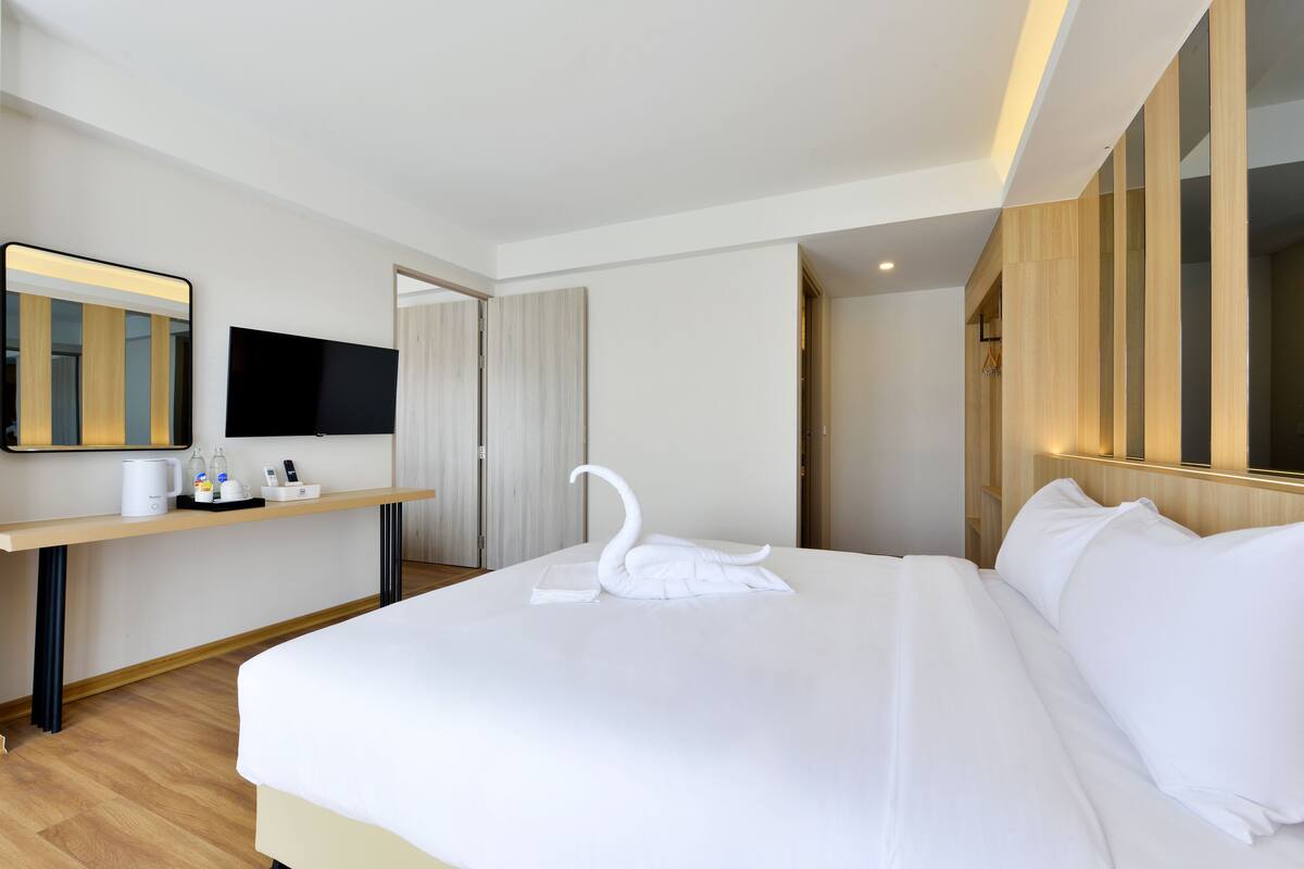 Ein Hotelzimmer mit einem aufgeräumten Bett, einem Flachbildfernseher, einem Holztisch und einem Spiegel.