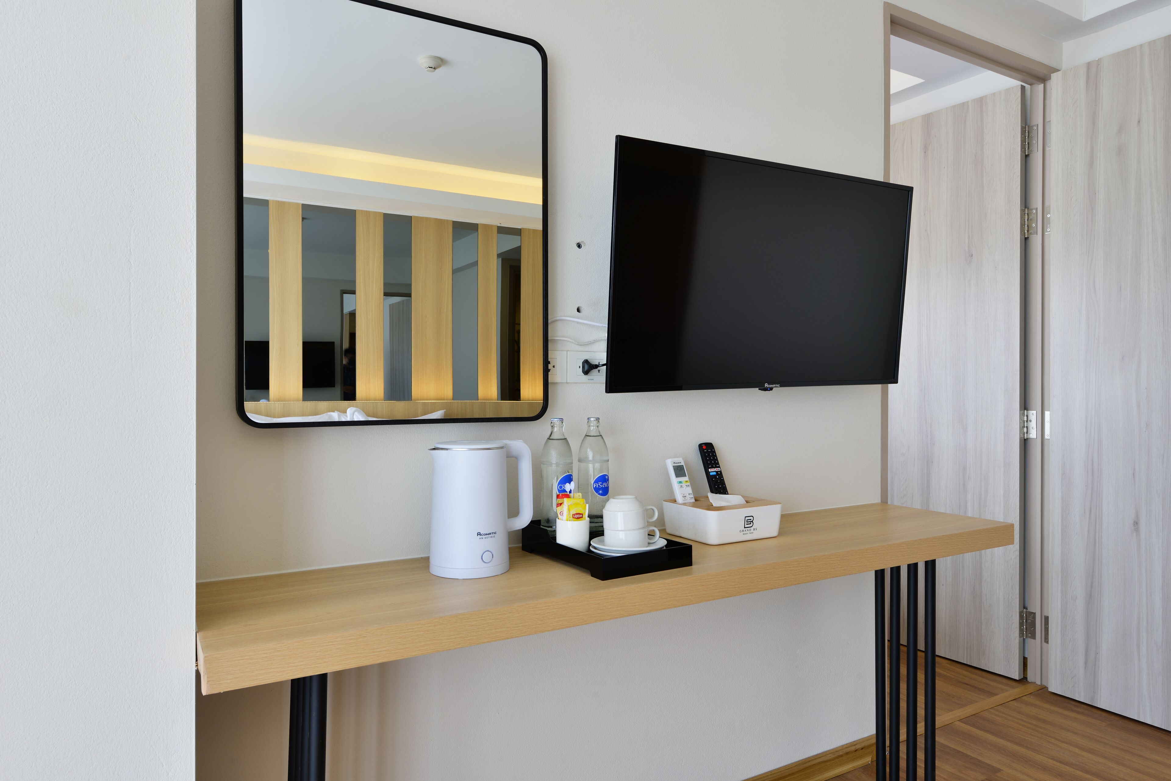 Habitación de hotel con una consola de madera, un televisor de pantalla plana, una cafetera y una bandeja con botellas y una taza.