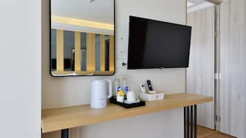 Habitación de hotel con una consola de madera, un televisor de pantalla plana, una cafetera y una bandeja con botellas y una taza.