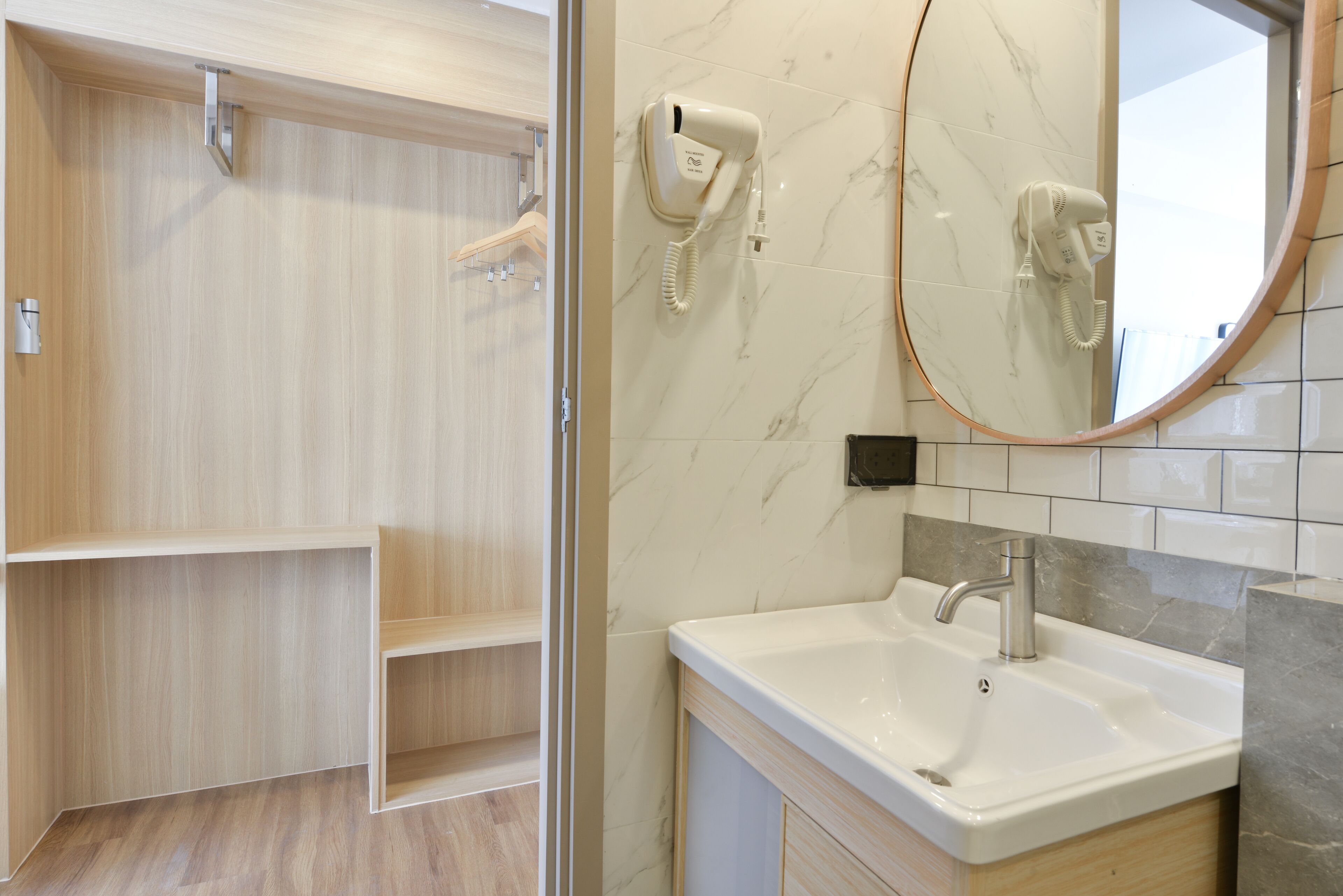 A bathroom with a wooden vanity, a white sink, and a marble-tiled wall.