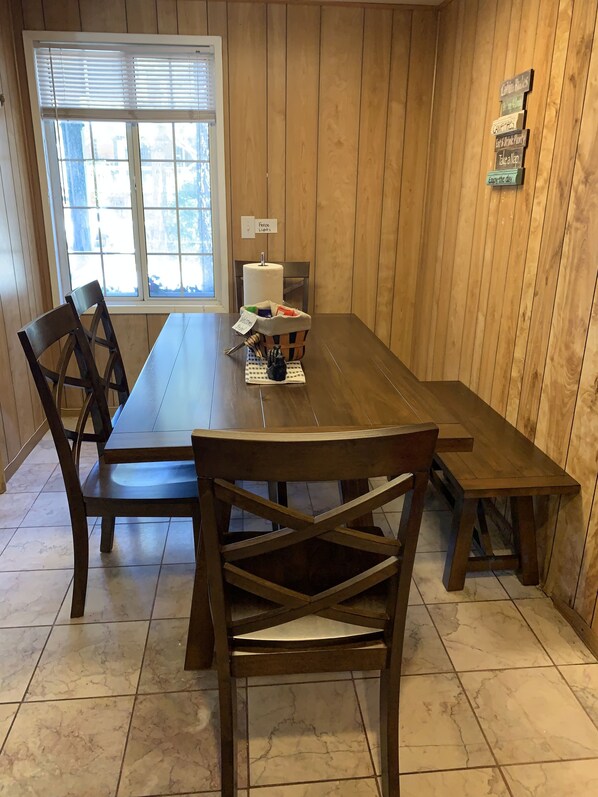 Une pièce aux murs lambrissés, comprenant une table à manger, des chaises, une bougie et un panneau affichant les règles.