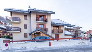 A multi-story building with balconies, a car parked in front, and a snow-covered ground. - South Studio 4 pers. Pets allowed (Valloire)