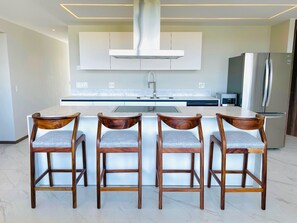Una cocina moderna con una isla central, taburetes de bar, un refrigerador de acero inoxidable y un horno empotrado.