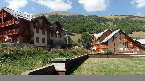 A traditional chalet-style building with multiple balconies, set against a backdrop of green hills and a clear sky. - Studio 2 cabins 4 pers. pets allowed, private parking (Valloire)