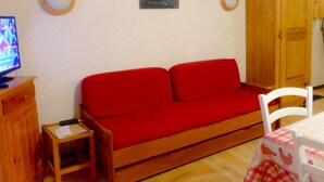 A small, cozy room with a red sofa, a wooden cabinet, a small table, and a television. - Studio 2 cabins 4 pers. pets allowed, private parking (Valloire)