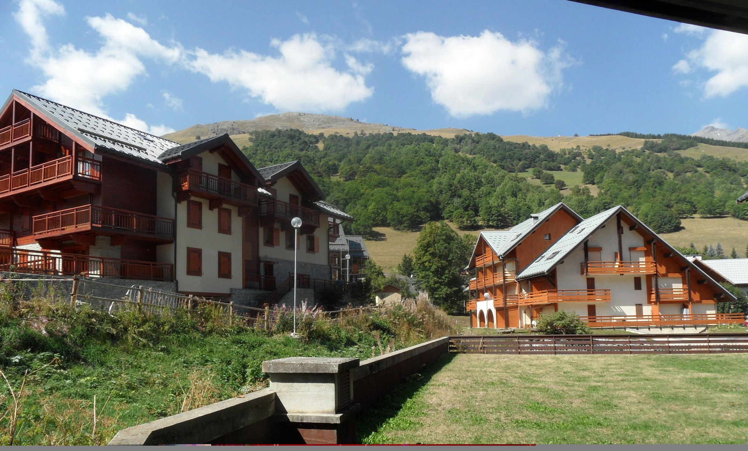 Un bâtiment de style chalet traditionnel, doté de nombreux balcons, qui se détache sur un paysage de collines verdoyantes et d’un ciel dégagé.