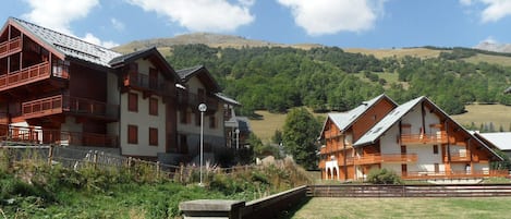 Un bâtiment de style chalet traditionnel, doté de nombreux balcons, qui se détache sur un paysage de collines verdoyantes et d’un ciel dégagé.
