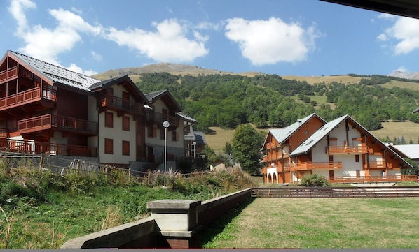 A traditional chalet-style building with multiple balconies, set against a backdrop of green hills and a clear sky.