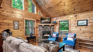 A cozy cabin interior with a stone fireplace, wooden walls, and a comfortable seating area.
