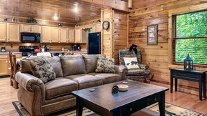 A cozy cabin interior with a wooden interior, a leather sofa, a dining table, and a kitchen area with wooden cabinets and appliances.