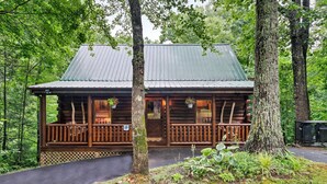 A log cabin with a porch, surrounded by trees.