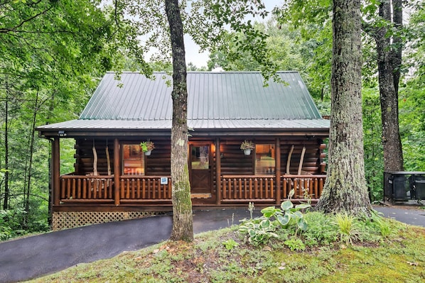 A log cabin with a porch, surrounded by trees.