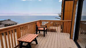 Une terrasse en bois avec deux tables et des chaises, donnant sur une plage et l’océan.