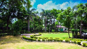 A well-maintained garden with manicured lawns, a curved pathway, and a building with a red roof in the background. - TGI Insignia Resort & Villa's (Bhopal)