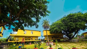 A courtyard with yellow buildings, a palm tree, and a playground. - TGI Insignia Resort & Villa's (Bhopal)