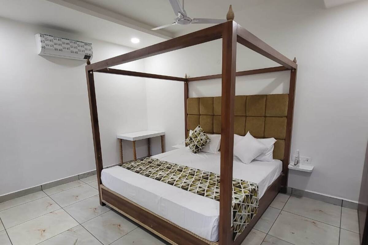 A four-poster bed with a wooden frame and a tufted headboard, a bedside table, and a nightstand with a lamp.