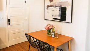 Un comedor con una mesa de madera, sillas negras, un florero con flores rosadas, una botella de vino y una copa.