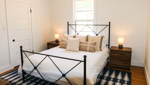 Un dormitorio con una cama, dos mesitas de noche, una ventana y una puerta.