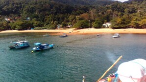 A coastal scene with boats on calm water, a sandy beach, and a forested hill in the background. - Big Island Longa Beach. (Angra dos Reis)