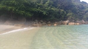 A beach with clear water, sandy shore, and a rocky cliff with dense foliage. - Big Island Longa Beach. (Angra dos Reis)