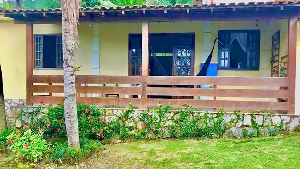 A house with a wooden fence, a garden with various plants, and a clear view of the house's exterior. - Big Island Longa Beach. (Angra dos Reis)