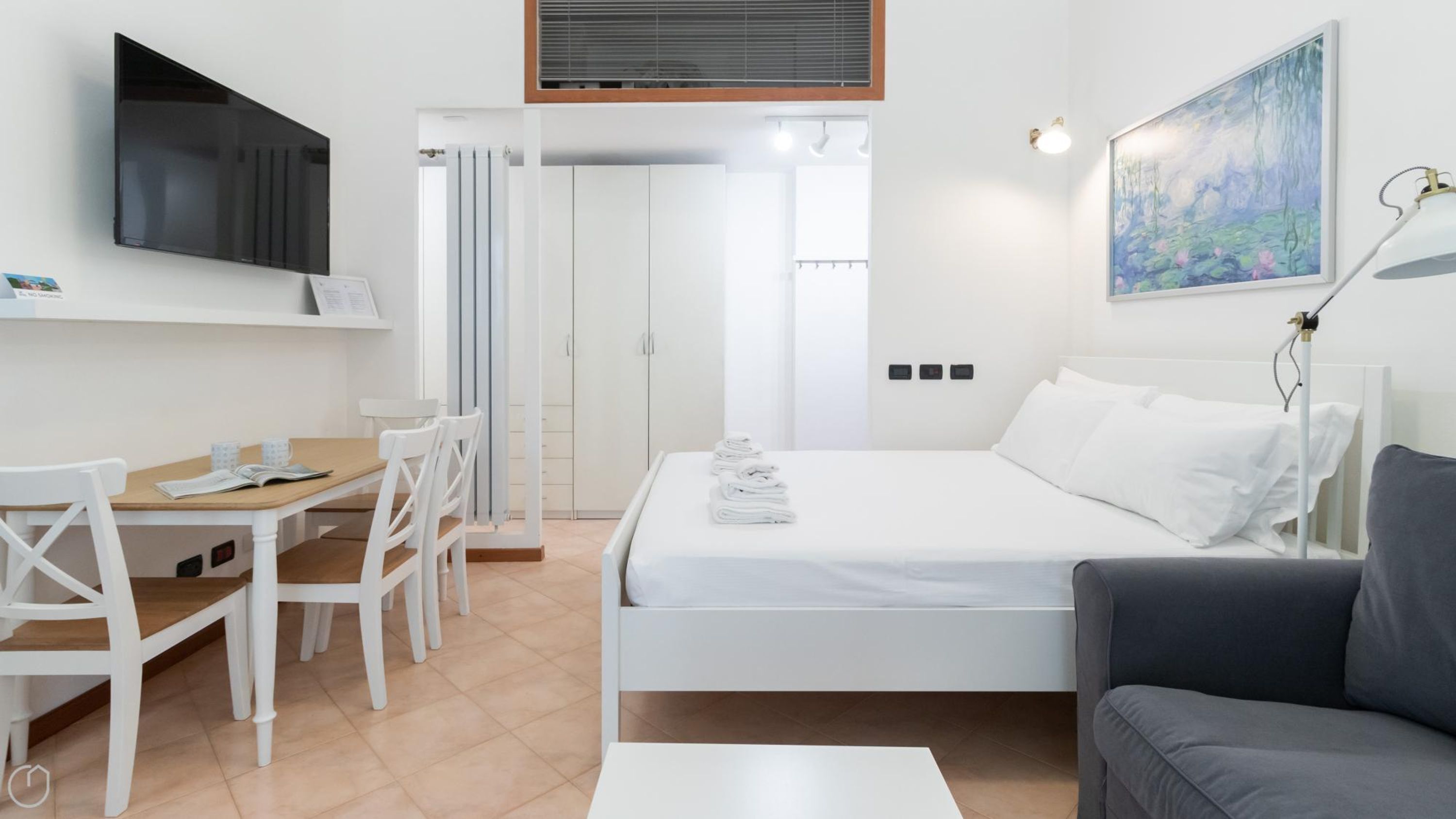 A hotel room with a bed, a desk, chairs, a TV, a painting, and a lamp.