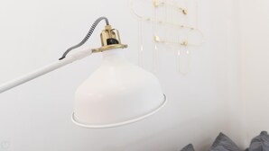 Une lampe de bureau blanche, dotée d’un col flexible et d’un pied de couleur dorée, fixée à un mur blanc.