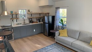 Une cuisine compacte avec des meubles gris, un réfrigérateur noir et un coin repas comprenant une table ronde et des chaises.
