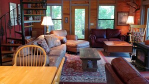 L’intérieur chaleureux d’un chalet avec un escalier en bois, des canapés en cuir, une table à manger en bois et une cheminée.