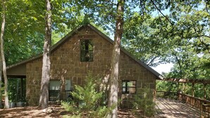Un bâtiment en pierre doté d’une terrasse en bois et d’un petit arbre devant.