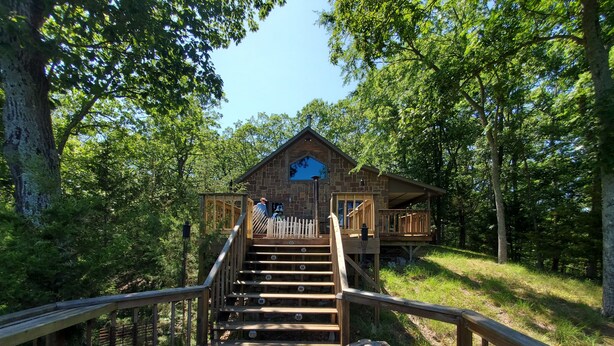 Une cabane en bois avec un escalier menant à une terrasse, entourée d’arbres.