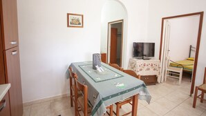 Ein kleiner, ordentlicher Raum mit Esstisch, Stühlen, Fernseher und Bett.