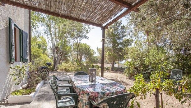 Eine Terrasse im Freien mit einem runden Tisch und Stühlen, umgeben von Bäumen und einem Gebäude.
