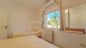 Ein Schlafzimmer mit Bett, einem Fenster mit Vorhängen, einem Heizkörper und einem Spiegel an der Wand.