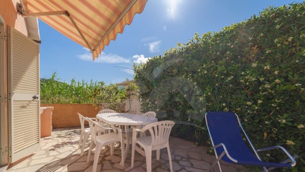Eine Terrasse im Freien mit Tisch und Stühlen, ein blauer Stuhl und ein Streifenmarkise.