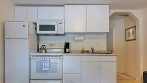 Een kleine keuken met witte kastjes, een magnetron, een fornuis en een koelkast.