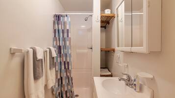 Een badkamer met een douche, wastafel, spiegel en handdoekhouder.