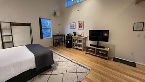 A bedroom with a bed, a desk, a TV, and a window.