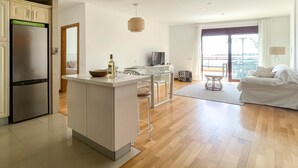 Uma cozinha moderna com uma ilha central, uma área de refeições com mesa e cadeiras, um sofá e uma varanda com vista.