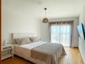A bedroom with a bed, bedside table, lamp, and a large window with curtains. - Sosego Sun by Best Holidays Fuerteventura (Corralejo)
