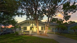 Une maison à deux étages avec un porche, entourée d’arbres et sous un ciel dégagé.