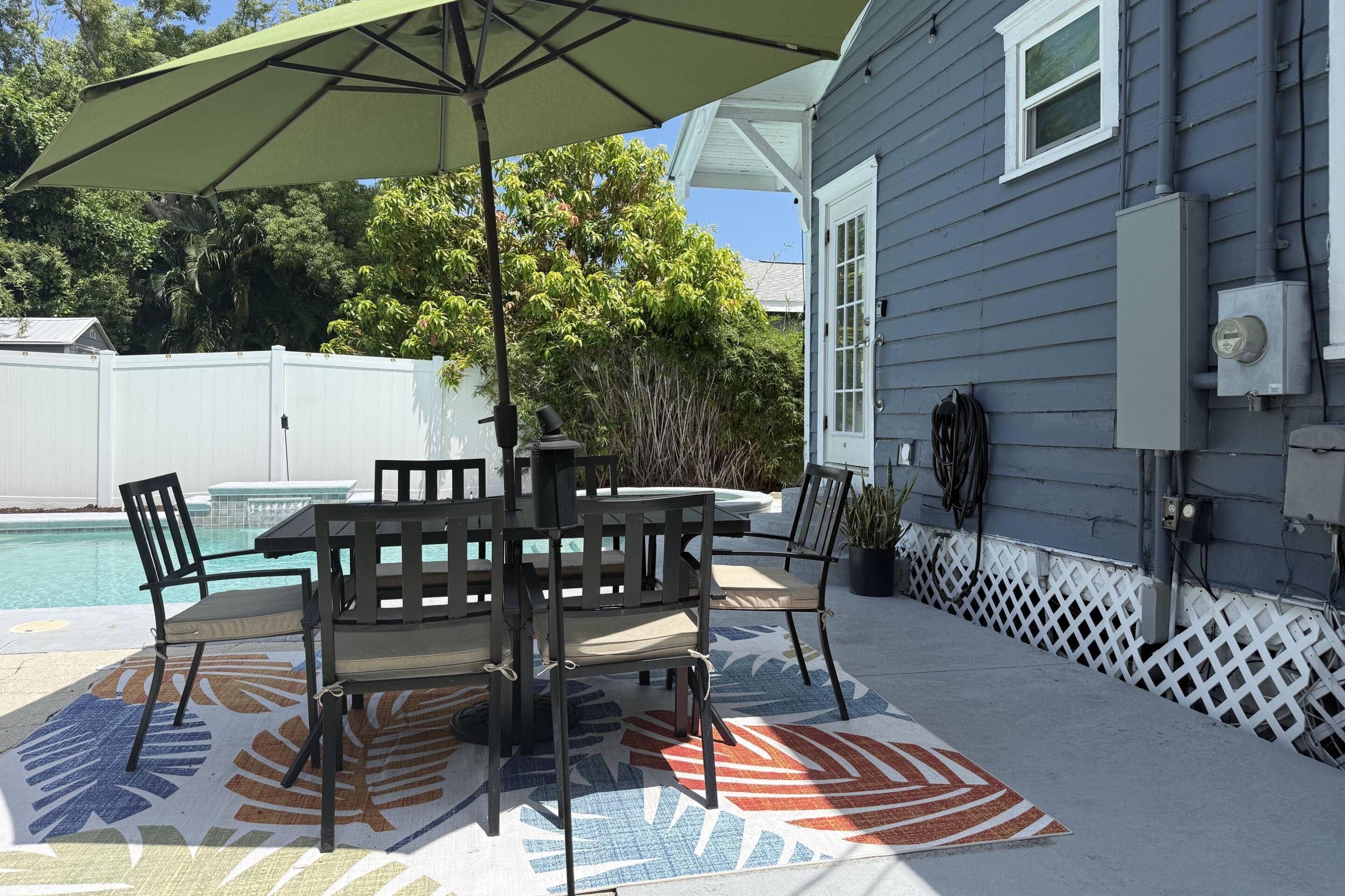 A patio with a table and chairs, a pool, and a covered area with an umbrella.