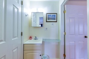 A bathroom with a white sink, a mirror, a framed picture, and a glass shelf.