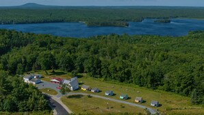 An aerial view of a small, rural community with a cluster of houses near a large body of water, surrounded by dense forest. - Clean & Cozy 1BR Apt#6 w/Full Kitchen & Private Bath (Ellsworth)