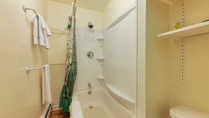 A bathroom with a bathtub, a shower, and a toilet. There are towels hanging on a rack and a shelf with toiletries. - Clean & Cozy 1BR Apt#6 w/Full Kitchen & Private Bath (Ellsworth)