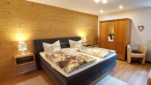 Een slaapkamer met een houten wand, een grote kast, een bed met bloemenbeddengoed, een stoel en een raam met uitzicht.
