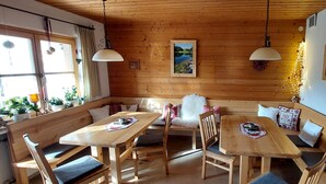 Een houten interieur met een houten bank, tafels en stoelen. Er hangen lampen en aan de muren bevinden zich afbeeldingen in lijsten.